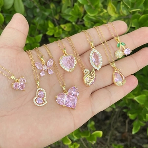 Gold necklaces with pink heart and butterfly pendants held in hand over green background