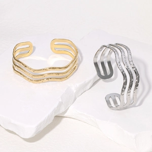 Minimalist 18K gold and silver plated stainless steel wave bangles on stone pedestals