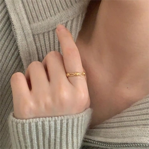 Close-up of golden hollow heart-shaped open ring shown on finger with soft knit background