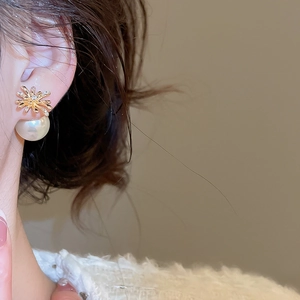 Close-up of gold fireworks earrings with zircon and large round pearl on ear model