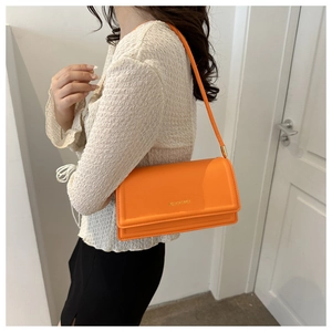 Detail van een feloranje schoudertas met goudkleurig logo-reliëf en slanke leren riem