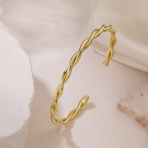 Minimalist twisted gold bangle in a stackable design featuring a smooth metallic finish
