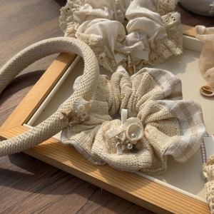 Detail of beige linen hairband and shell accessories on a wooden tray in sunlight