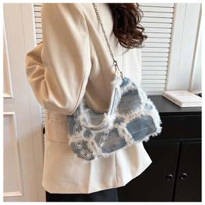 Detail of denim shoulder bag featuring frayed fringe texture and acrylic chain strap