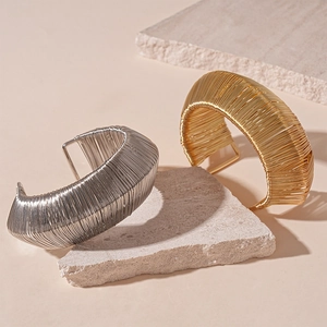 Woven geometric metal cuff bracelet in gold and silver finish on a stone surface