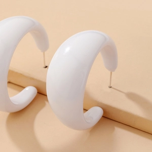 Detailed view of white resin C-shaped hoop earrings on a minimalist beige display stand