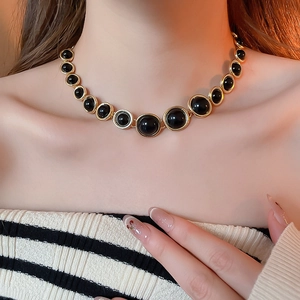 Close-up of a vintage-style gold necklace with black oval resin beads on model neck