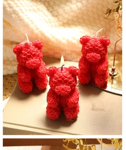 Detailed view of red rose bear candles on a book with one candle lit and flickering