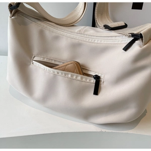 Close-up of beige nylon tote bag showing front zipper pocket and adjustable strap detail