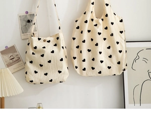 Detail view of textured canvas shoulder bag and tote with black heart pattern prints.