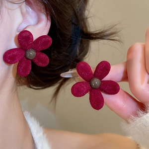 Macro detail of red flocked flower stud earrings with a soft velvet texture on a model