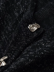 Dettaglio macro di cardigan in maglia nera con fili di lurex e bottoni in metallo