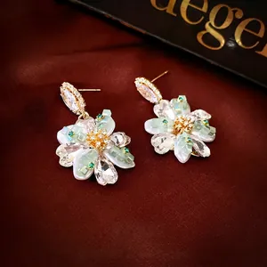 Elegant gold flower earrings with crystals and green beads on a luxury silk background