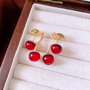 Macro view of cherry stud earrings with red stones and gold branch on white velvet