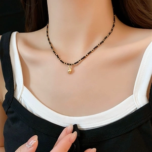 Detail of shell pendant on black and gold beaded necklace worn on neck