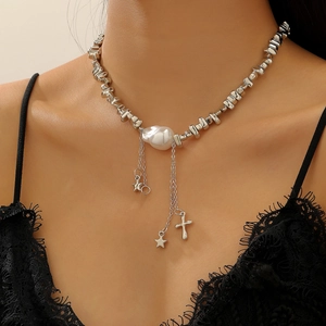 Détail du collier de perles baroques avec breloques étoile et croix sur robe en dentelle