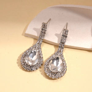 Détail de boucles d'oreilles goutte argentées avec strass brillants sur socle blanc