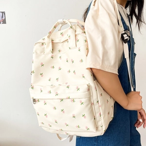 Floral canvas backpack in cream with pink flower print worn on person with white wall backdrop
