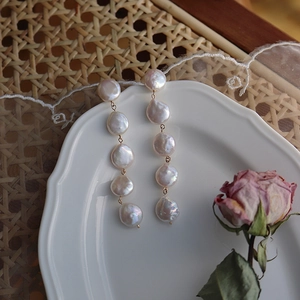 Detailed shot of long baroque pearl earrings with five flat freshwater pearls on gold chain