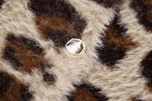 Nahaufnahme eines goldenen unregelmäßigen Knopfes auf einem Strickcardigan mit Leoprint