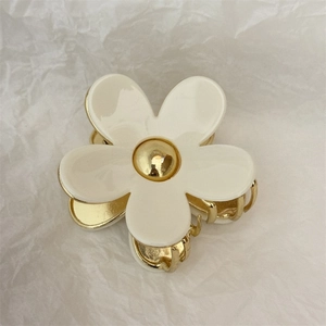 Macro view of cream floral hair claw with gold metal center on textured paper