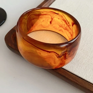 Macro detail of a vintage amber marble resin bangle on a textured wooden tray