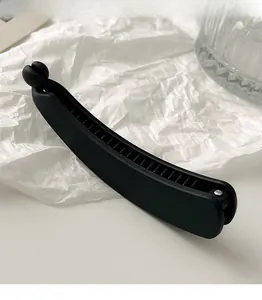 Close-up of matte black banana hair clip with non-slip teeth on textured white paper