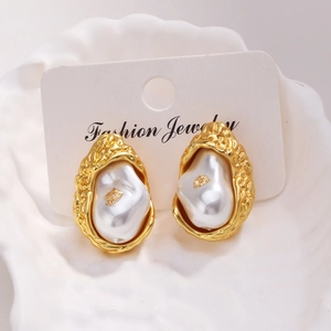 Détail macro de boucles d'oreilles en or 18 carats avec perle baroque et feuille d'or