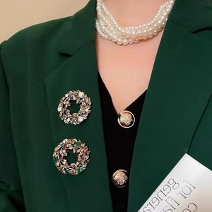 Detail view of vintage baroque flower brooches with pearls on a dark green blazer jacket