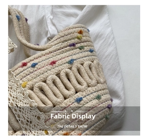 Detailed view of handmade woven straw bag with colorful pom-poms and white lace trim