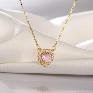 Macro view of heart pendant with pink zircon and gold chain on white silk fabric