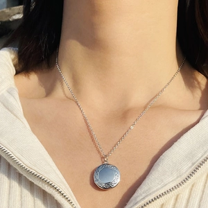 Close-up of a silver engraved round charm pendant necklace worn on a model's neck