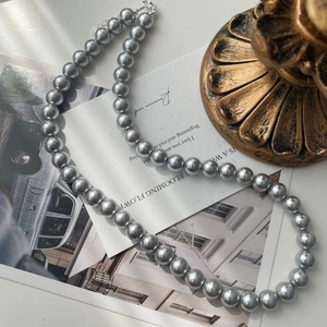 Detailed view of grey faux pearl necklace with round beads and silver clasp on decorative cards