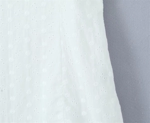 Detailed close-up of white floral eyelet embroidery and stitching on fine cotton fabric
