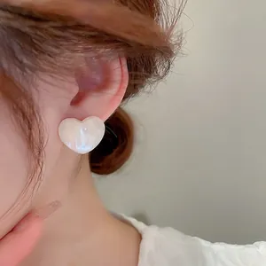 Elegant acrylic heart earrings with iridescent pearl finish worn by a model
