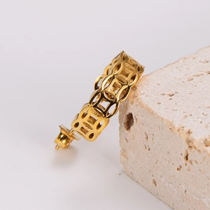 Elegant gold cutout coin stud earrings displayed on a light textured stone background