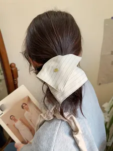 Detail of a vintage striped bow hair scrunchie with a gold metal plate on a model