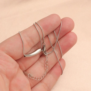 Close-up of a silver curved tube pendant necklace with lobster clasp held in a hand