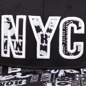 Close-up of NYC embroidery and graffiti newspaper texture on black flat brim hip hop cap