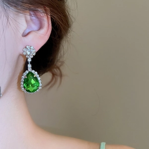 Dettaglio di eleganti orecchini in argento con cristallo a goccia verde e strass brillanti