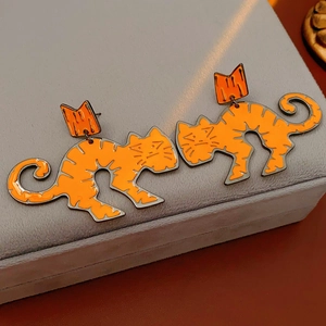Detail of orange enamel cartoon cat earrings featuring a sleek arched body design