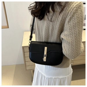 Detail of a black leather saddle bag featuring a stylish gold metal bar closure