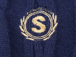 Macro shot of gold embroidery on navy blue knit fabric with wheat wreath and letter S