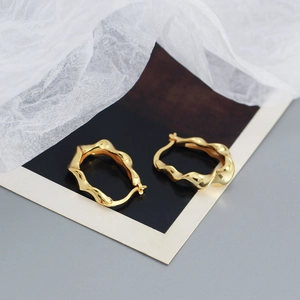 Detailed view of golden irregular wavy earrings on dark card with soft white mesh fabric