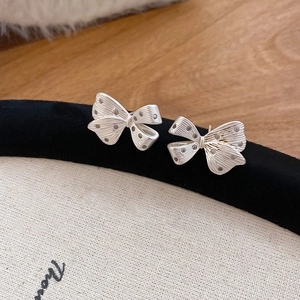 Detailed view of silver bow-knot earrings with brushed texture on a velvet stand
