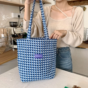 Blue and white checkered woven tote bag with purple label shown in a cafe setting