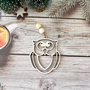 Detail of laser-cut owl wooden ornament with twine loop on rustic pine background