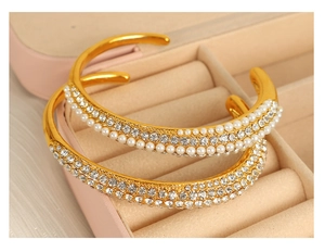 Macro shot of gold open cuff bracelets with pearls and rhinestones on a pink jewelry box