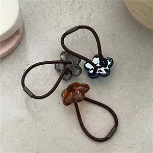 Three-piece set of acrylic flower hair ties in amber, gray, and blue on stone background