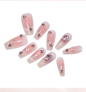 Close-up of pink gradient press-on nails with heart rhinestones and oval gemstones